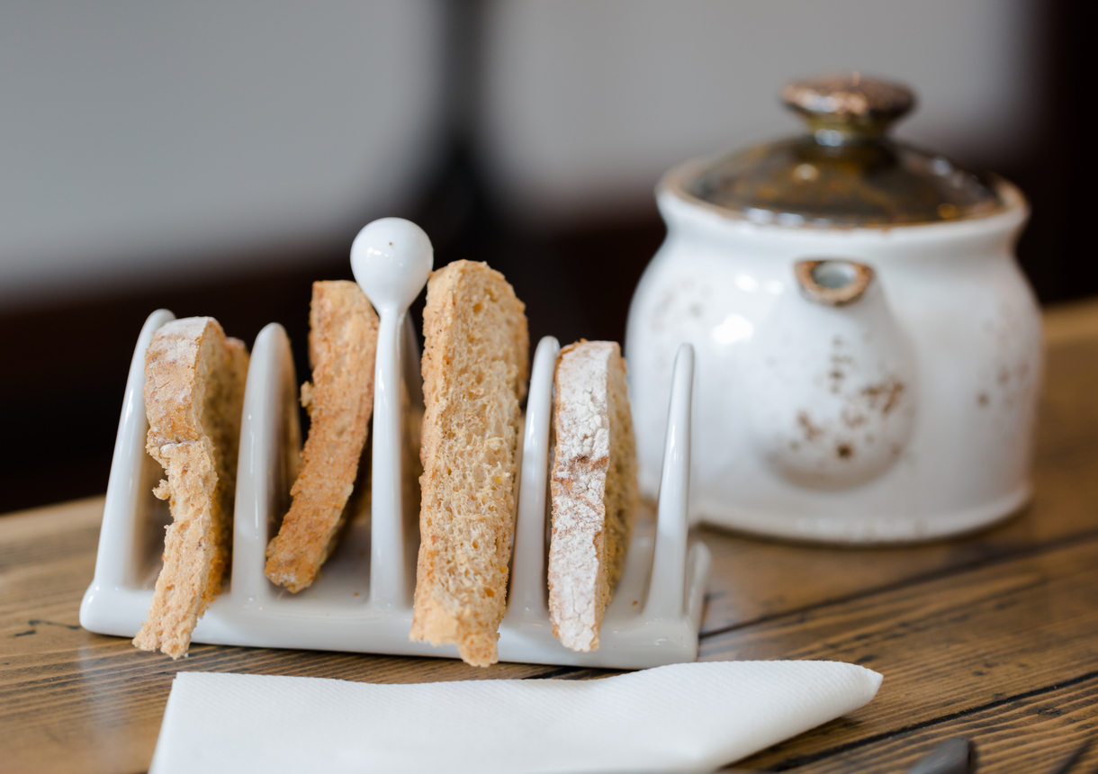 Four slices of toasted bread in vintage style toasts holder on wooden table close up