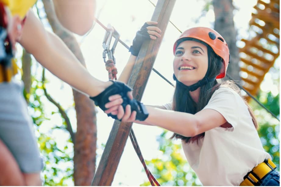 A person wearing a helmet and holding hands with another person in a rope park